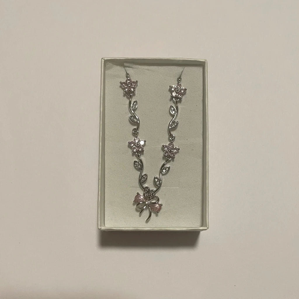 Collier de couleur argentée à fleurs rose pâle, feuillage scintillant et motif nœud central