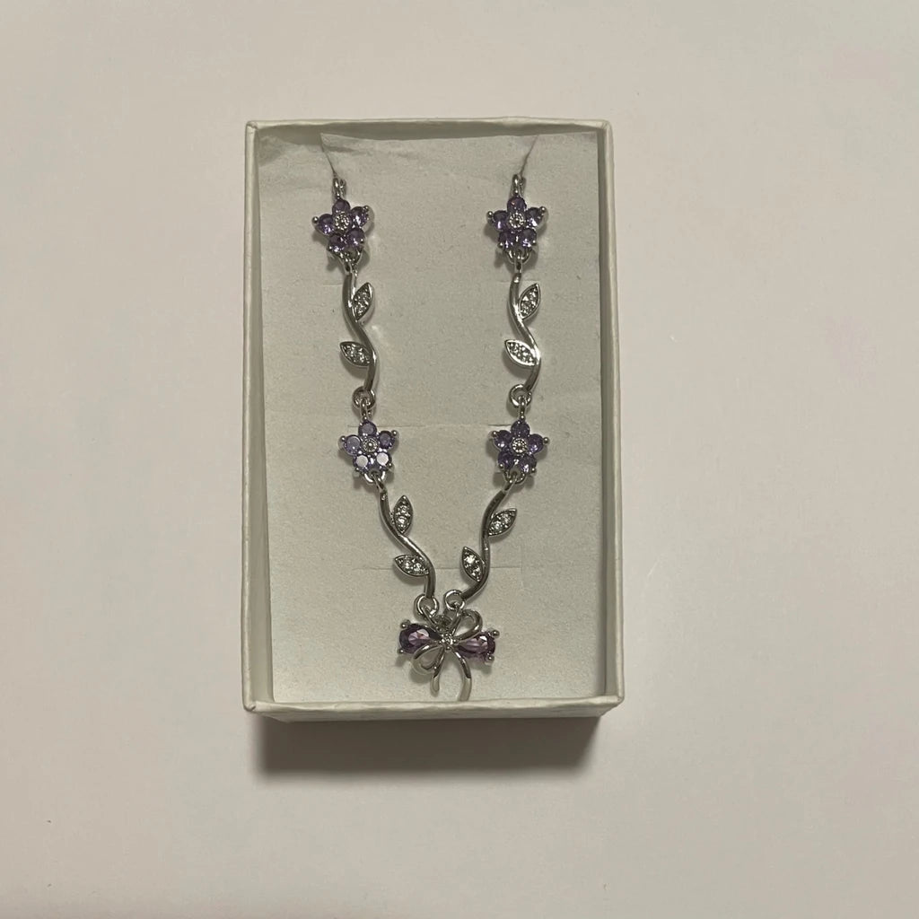 Collier de couleur argentée à fleurs violettes, feuillage scintillant et motif nœud central