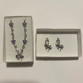 Collier argenté à fleurs violettes et boucles d’oreilles à nœuds violets, présentés dans deux écrins clairs