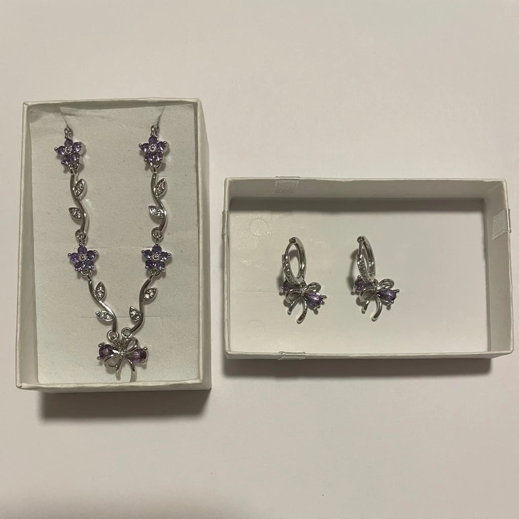 Collier argenté à fleurs violettes et boucles d’oreilles à nœuds violets, présentés dans deux écrins clairs