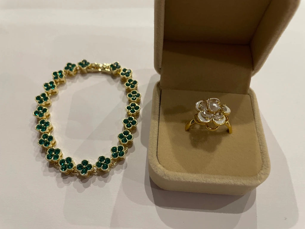 Bracelet doré à motifs trèfle vert et bague dorée à fleur blanche, présentés dans deux écrins