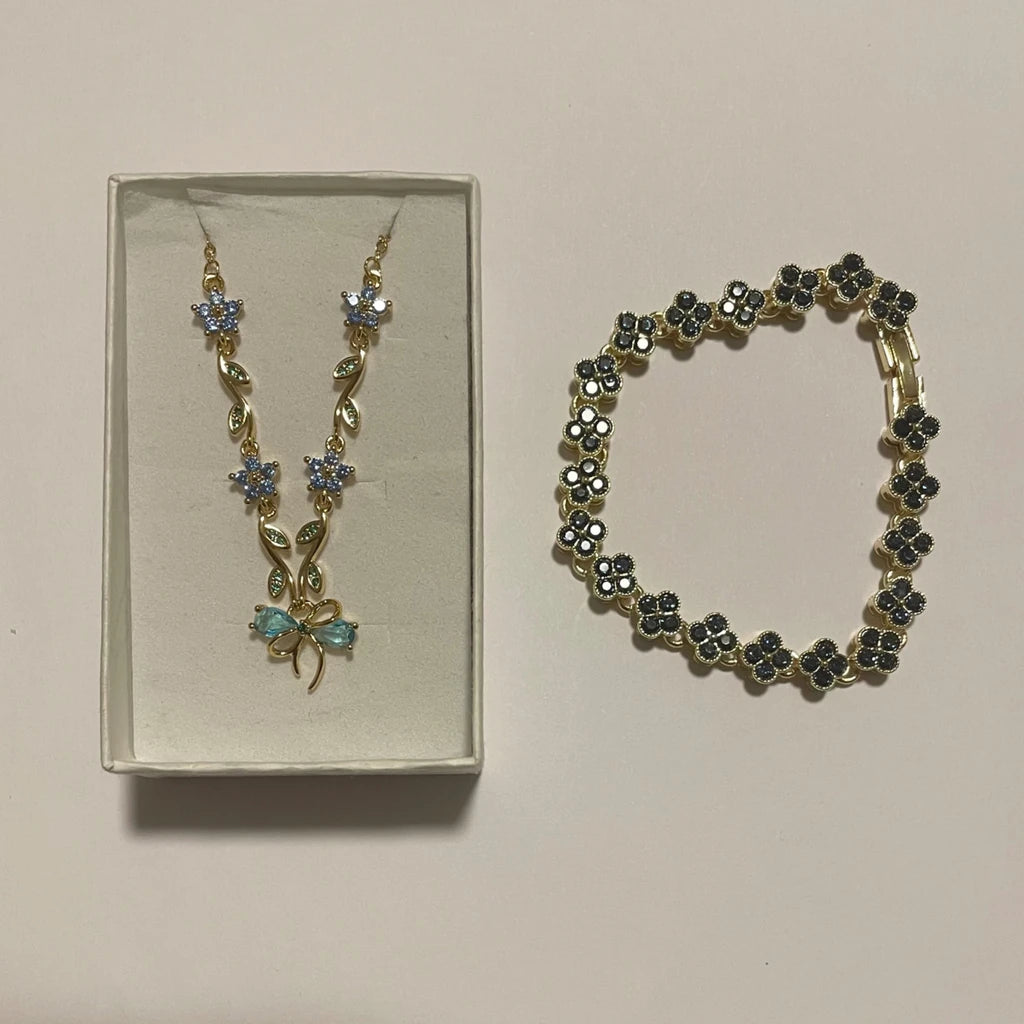 Collier doré à fleurs bleues et nœud turquoise, accompagné d’un bracelet à motifs trèfle foncés