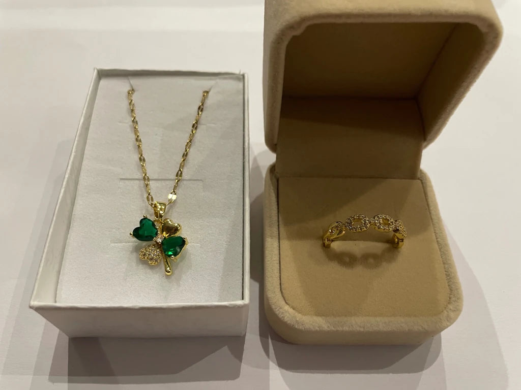 Collier doré à pendentif trèfle vert et bague dorée à maillons scintillants, présentés dans deux écrins