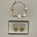 Bracelet doré à cinq fleurs roses et boucles d’oreilles florales roses et blanches présentées dans un écrin clair