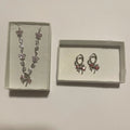 Collier argenté à fleurs rose pâle et boucles d’oreilles créoles à nœuds rose corail, présentés dans deux écrins clairs