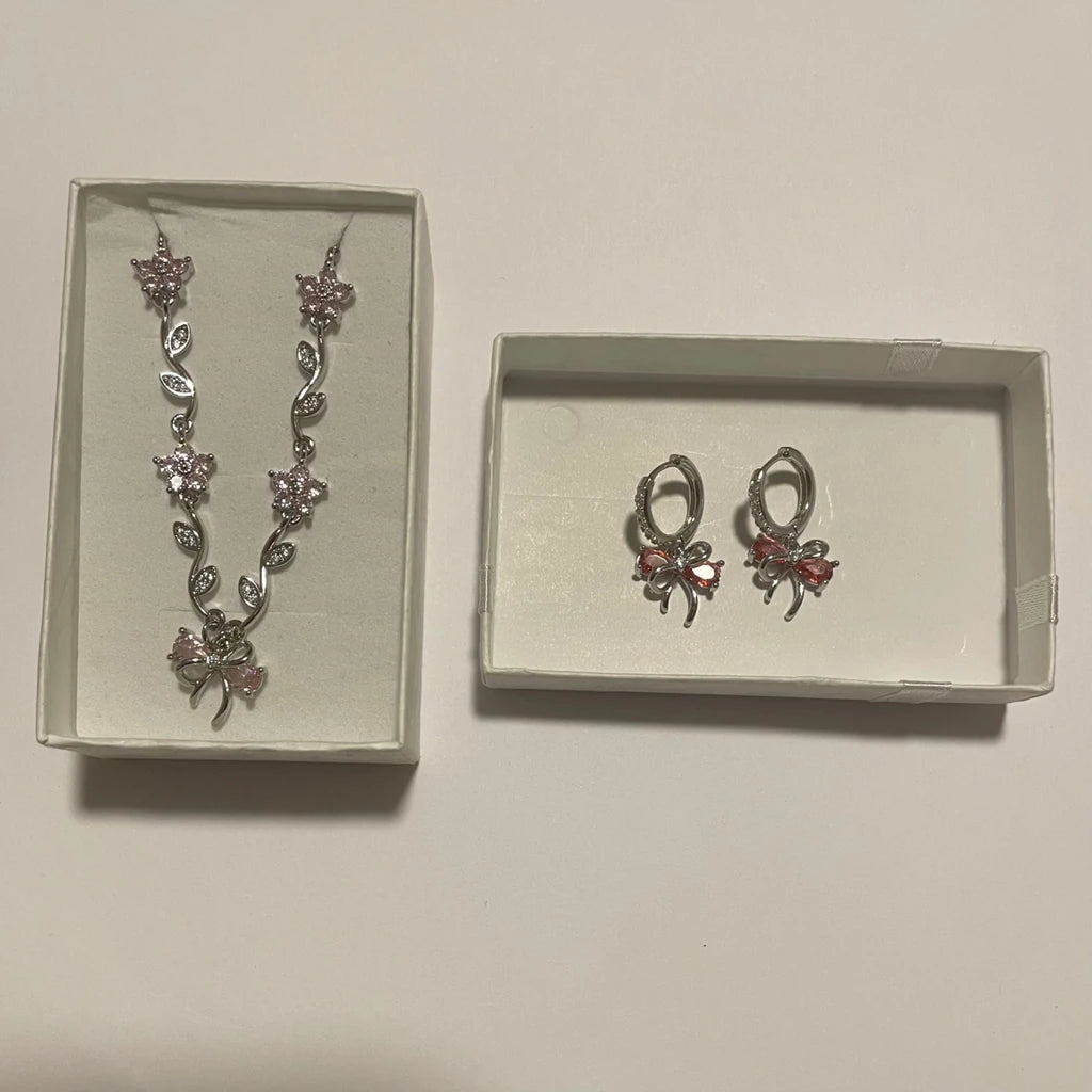 Collier argenté à fleurs rose pâle et boucles d’oreilles créoles à nœuds rose corail, présentés dans deux écrins clairs